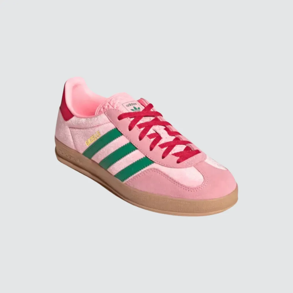 Tênis adidas Gazelle Indoor Glow Pink Court Green com cabedal em veludo rosa, sobreposições em camurça, detalhes em verde, perfil baixo clássico e solado de borracha, representando um sneaker retrô versátil para o lifestyle urbano.