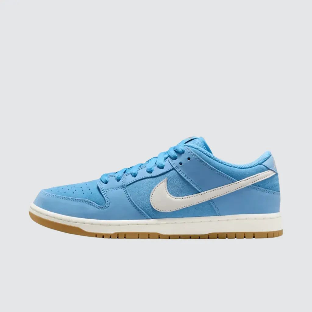 Tênis Nike Dunk Low SB University Blue Gum com cabedal azul em malha, camurça e couro, Swoosh branco, marca no calcanhar e solado de borracha gum, representando um sneaker de skate com forte identidade streetwear.