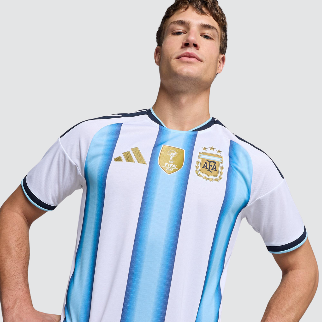 Camisa titular seleção argentina 2026 adidas branca com listras azul celeste e detalhes dourados, inspirada nos três títulos mundiais.