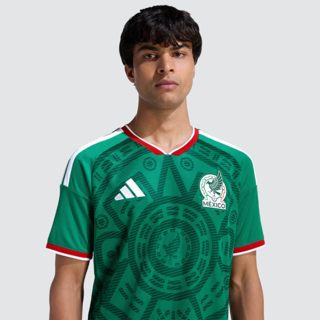 Camisa titular México 2026 em ambiente esportivo, destacando o verde vibrante, os grafismos culturais inspirados no uniforme de 1998 e a energia que simboliza o orgulho mexicano.