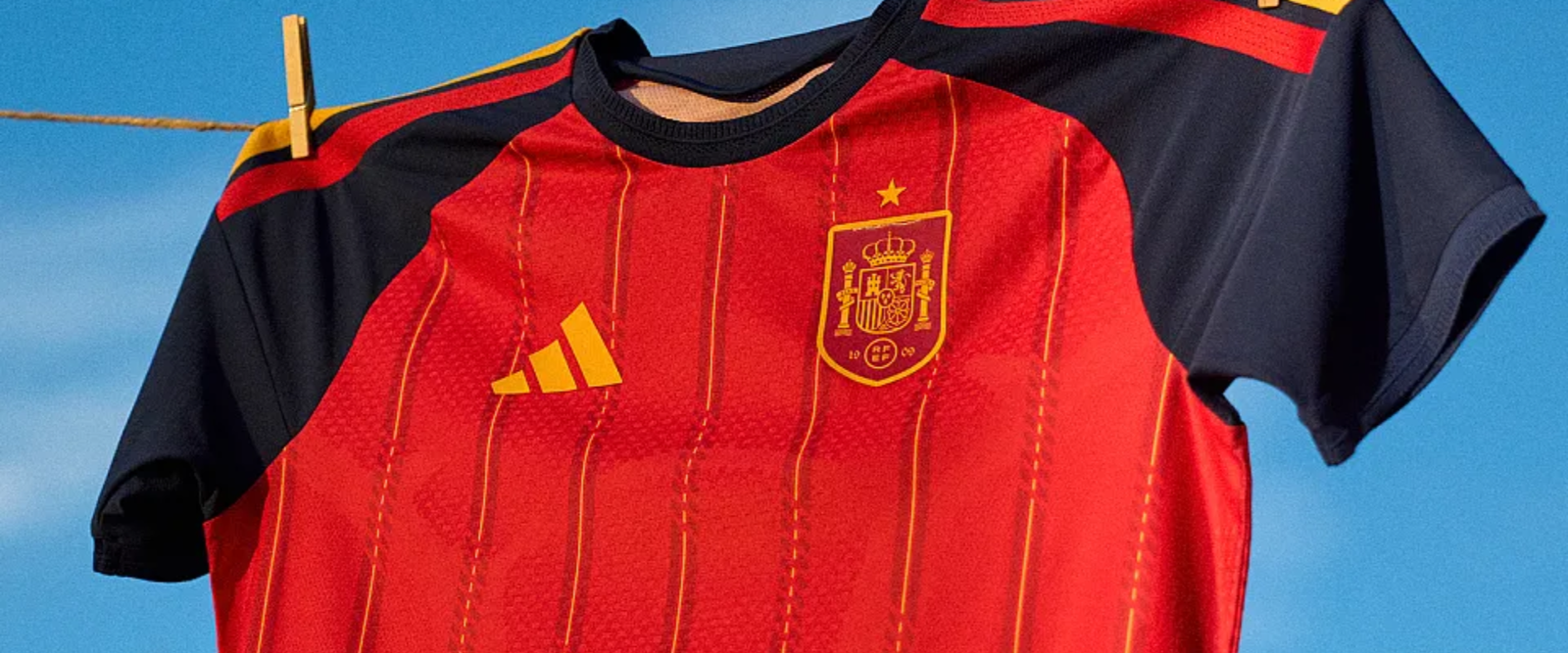 Camisa adidas Espanha titular 2026/27 vermelha com listras amarelas e gola azul-marinho, inspirada na La Roja.