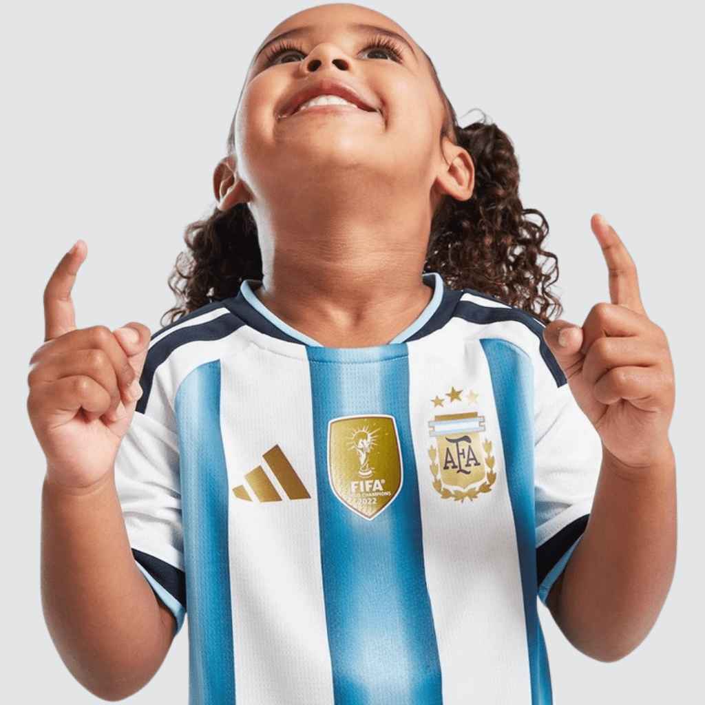 Conjunto infantil Argentina 2026 adidas branco e azul celeste com patch de tricampeão e calção azul-marinho.