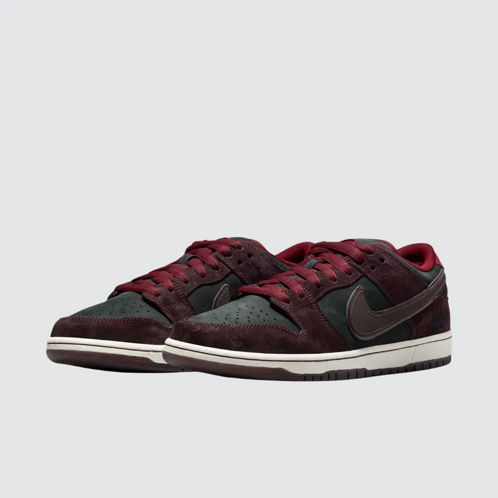 Tênis Nike RIOT Skateshop x Dunk Low SB Mahogany Dark Beetroot com cabedal em nobuck e camurça premium, tons vinho e verde escuro, Swoosh bordô com contorno brilhante, palmilha de cortiça artística e solado translúcido, representando uma colaboração entre cultura skate e herança urbana francesa.