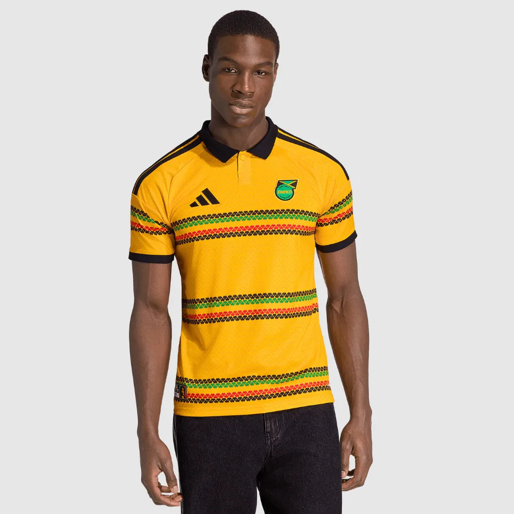 Camisa titular da Jamaica adidas 2026 amarelo-dourada com listras horizontais vermelhas e pretas, design inspirado na cultura rastafári e identidade caribenha