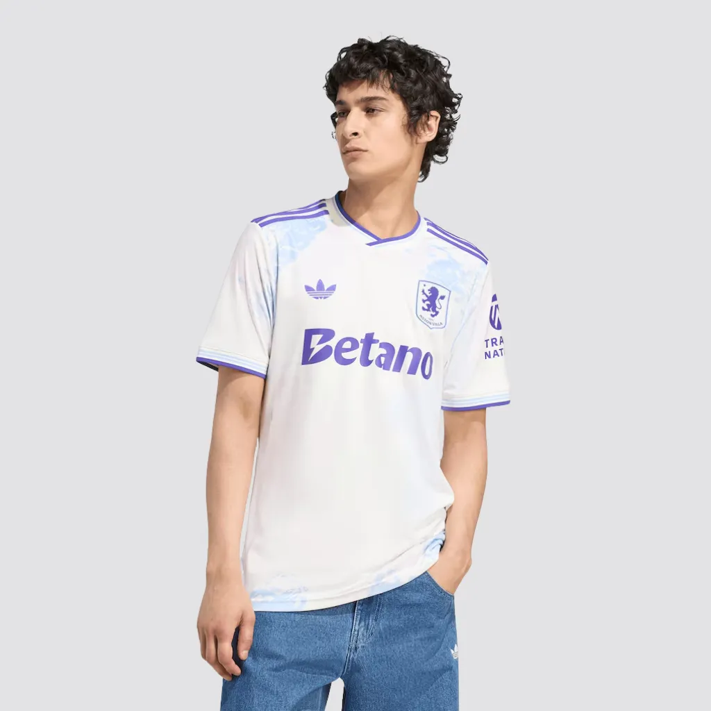 Camisa terceira do Aston Villa adidas 2025 2026 com grafismos inspirados em vitrais, base clara, detalhes bordô e escudo central do clube